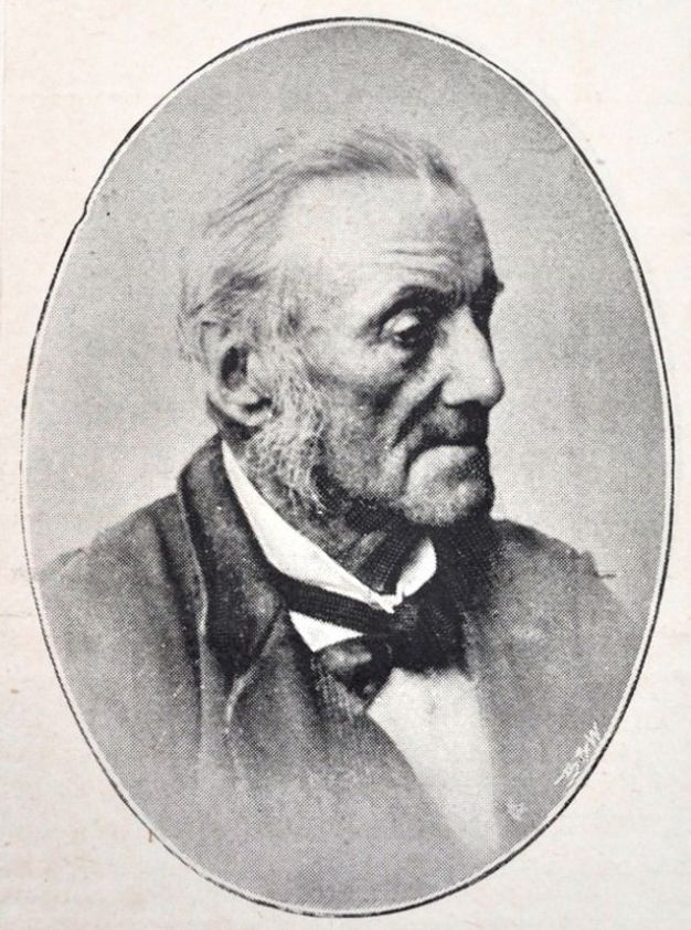 Black and white photograph. The head and shoulders of a man, Francis Alexander Skidmore, are set in an oval frame. He almost faces our right in profile and looks past a bumped nose with deep-set eyes under peaked brows. A deep wrinkle runs from the side of his nose nearly to the corner of his mouth under a high cheekbone. He has grey hair and mutton chops, and wears a white collar shirt, jacket, and black necktie. 